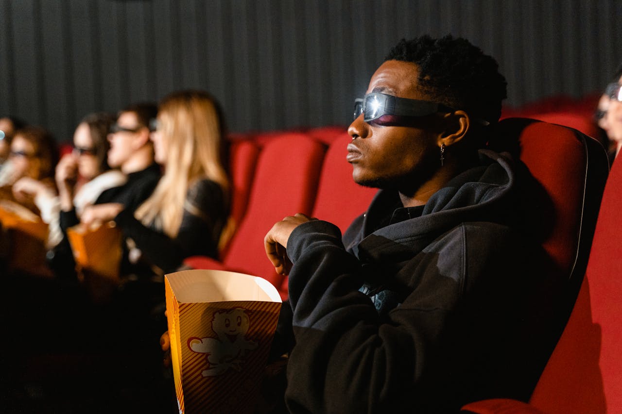 A group of adults in a cinema wearing 3D glasses watching a movie and eating popcorn.